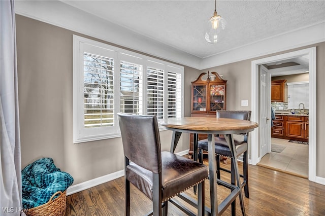 dining room with a textured ceiling, light wood-style flooring, and baseboards