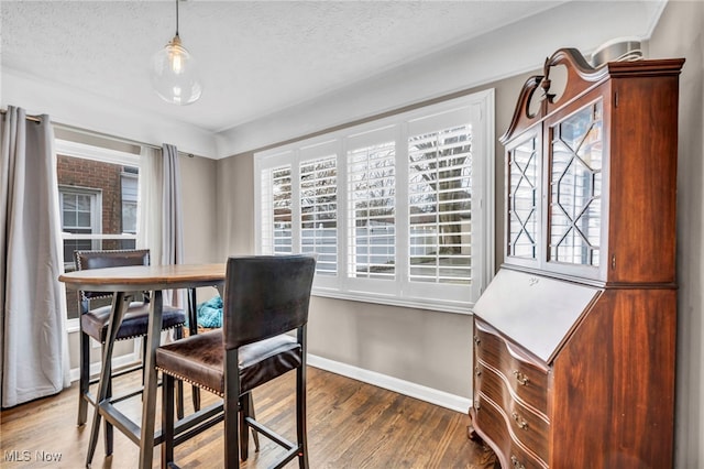 dining area with a textured ceiling, baseboards, and wood finished floors