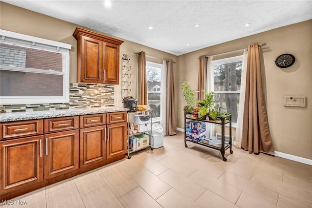 kitchen featuring backsplash, brown cabinetry, a textured ceiling, light stone countertops, and baseboards