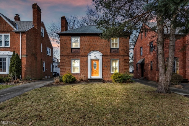 view of front of property featuring a front yard, brick siding, and a chimney