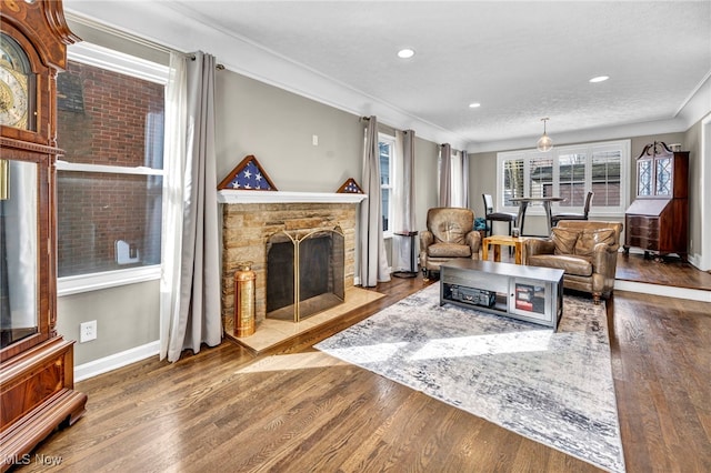 living area featuring a stone fireplace, recessed lighting, wood finished floors, baseboards, and crown molding