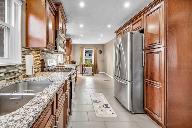 kitchen with tasteful backsplash, brown cabinetry, light stone countertops, stainless steel appliances, and light tile patterned flooring