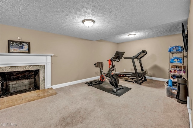 exercise area with a textured ceiling, baseboards, a fireplace with raised hearth, and carpet flooring