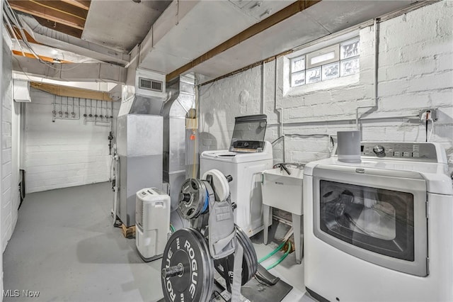 laundry area featuring laundry area, visible vents, heating unit, washer and clothes dryer, and concrete block wall