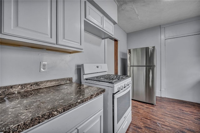 kitchen featuring dark wood-type flooring, freestanding refrigerator, white cabinetry, dark stone countertops, and white gas range oven