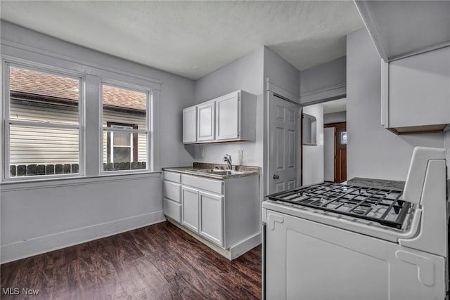 kitchen featuring white range with gas cooktop, baseboards, white cabinets, dark wood finished floors, and a sink