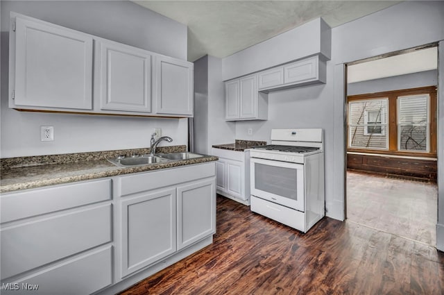 kitchen featuring dark wood-style flooring, a sink, white cabinets, white gas range, and dark countertops