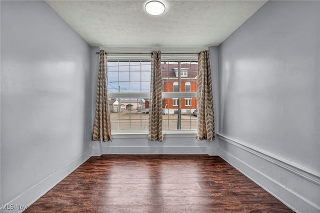 empty room with a textured ceiling, wood finished floors, and baseboards