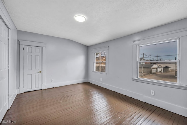 unfurnished room with a textured ceiling, baseboards, vaulted ceiling, and hardwood / wood-style floors