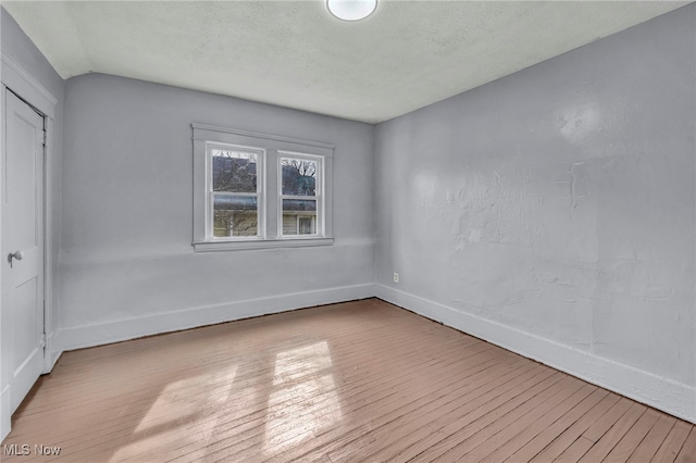 unfurnished room featuring lofted ceiling, wood-type flooring, a textured ceiling, and baseboards