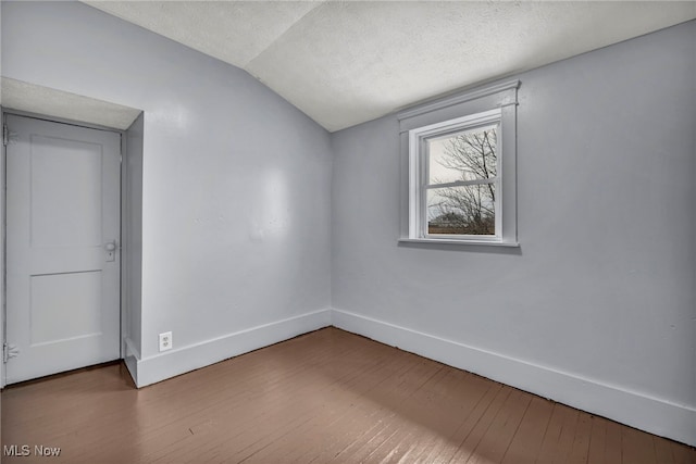 spare room featuring a textured ceiling, hardwood / wood-style floors, vaulted ceiling, and baseboards