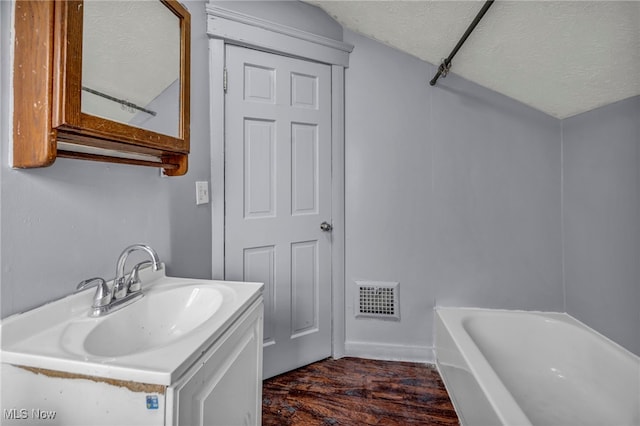 bathroom with visible vents, a tub, wood finished floors, a textured ceiling, and vanity