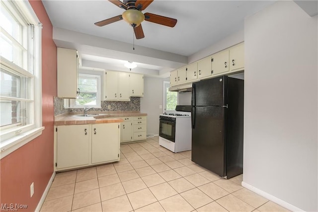 kitchen with cream cabinets, under cabinet range hood, range with gas cooktop, and freestanding refrigerator