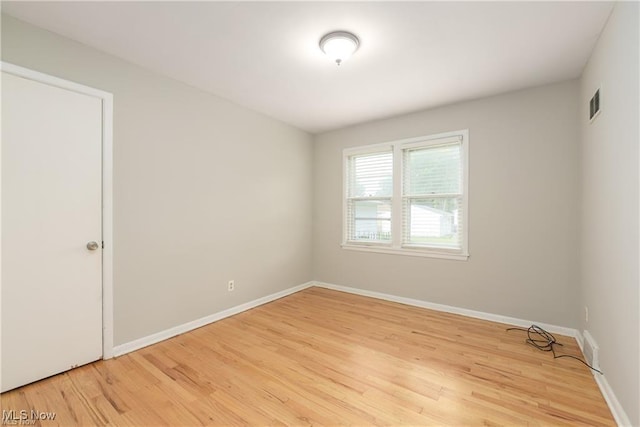 empty room with baseboards, visible vents, and light wood finished floors