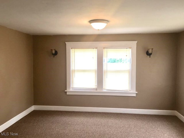 unfurnished room featuring dark carpet and baseboards