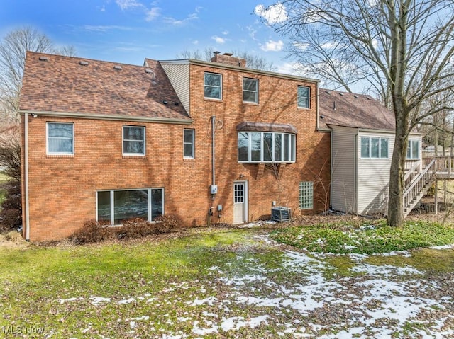 rear view of property with central air condition unit, a shingled roof, a lawn, and brick siding