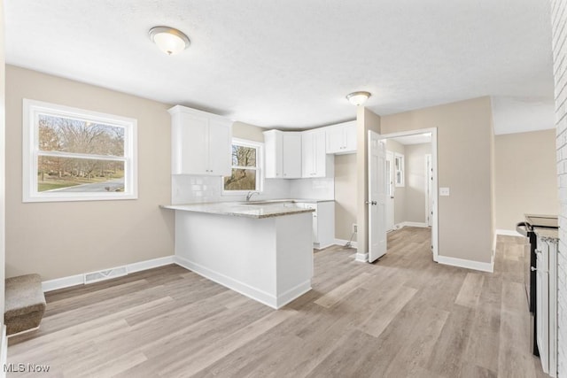 kitchen featuring visible vents, baseboards, a peninsula, light wood-type flooring, and white cabinetry