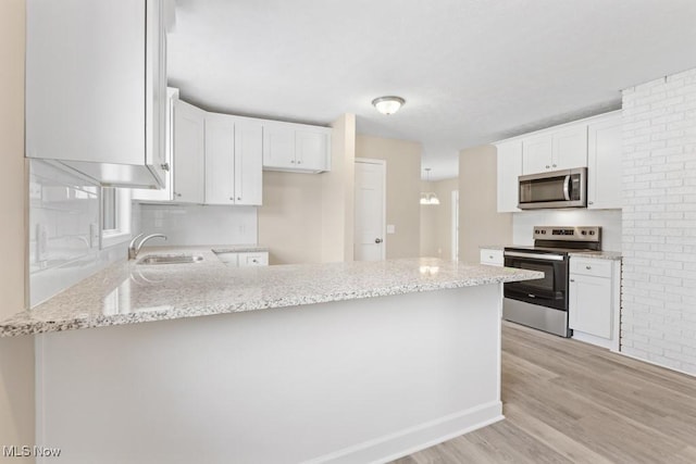 kitchen featuring light stone counters, light wood-style flooring, appliances with stainless steel finishes, a sink, and a peninsula