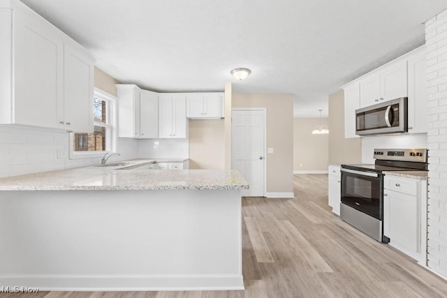 kitchen featuring light stone counters, light wood finished floors, appliances with stainless steel finishes, white cabinets, and a peninsula