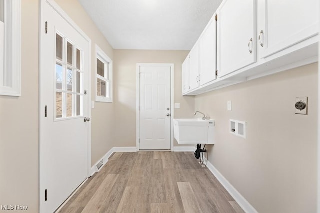 clothes washing area with hookup for a washing machine, cabinet space, light wood-style flooring, and baseboards