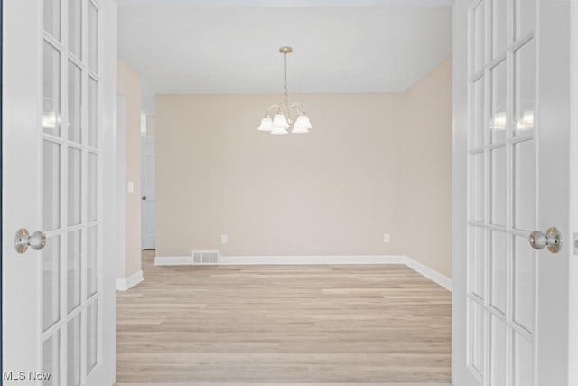 unfurnished room featuring light wood-type flooring, visible vents, baseboards, and an inviting chandelier