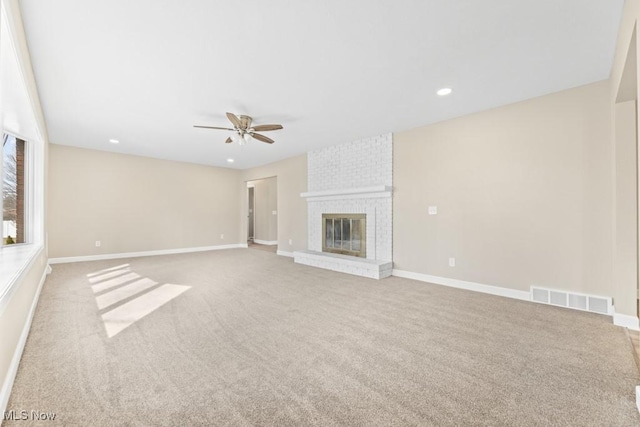 unfurnished living room with carpet, visible vents, a brick fireplace, ceiling fan, and baseboards