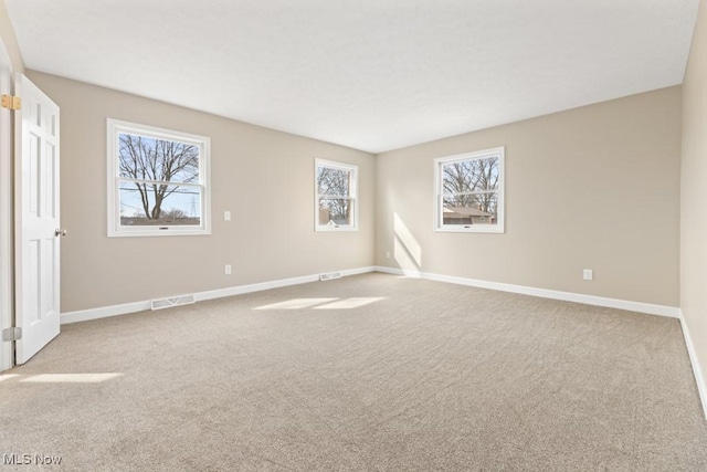 carpeted spare room with a healthy amount of sunlight, baseboards, and visible vents