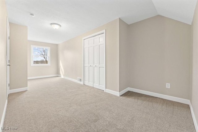 unfurnished bedroom with carpet flooring, visible vents, baseboards, vaulted ceiling, and a closet