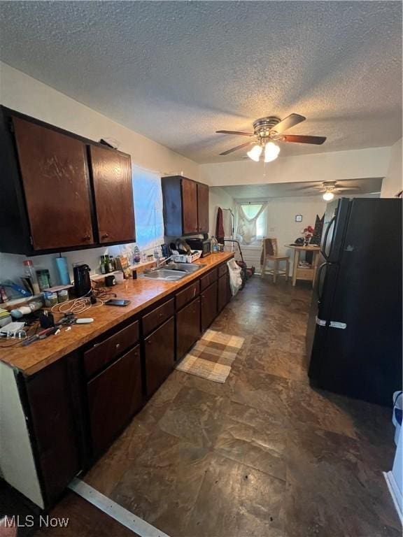 kitchen featuring light countertops, freestanding refrigerator, a sink, a textured ceiling, and dark brown cabinets