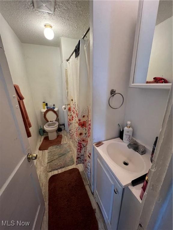 full bathroom with a textured ceiling, toilet, a shower with shower curtain, vanity, and visible vents