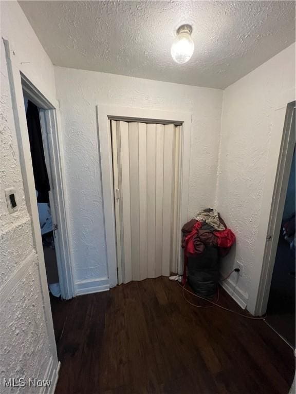 interior space with a textured ceiling, a textured wall, a closet, and wood finished floors