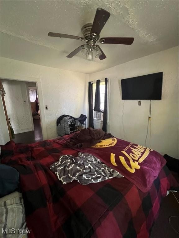 bedroom with a textured ceiling, ceiling fan, and a textured wall