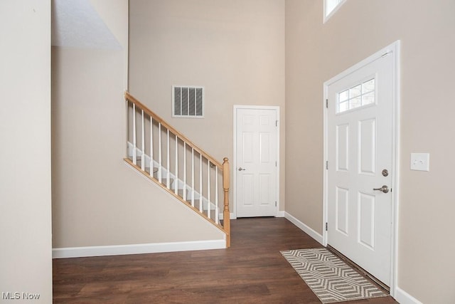 foyer with visible vents, baseboards, stairway, a towering ceiling, and wood finished floors