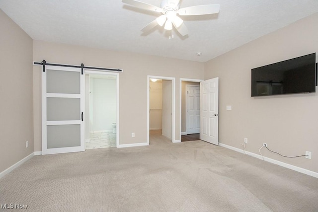 unfurnished bedroom with ensuite bathroom, a barn door, carpet floors, baseboards, and a spacious closet