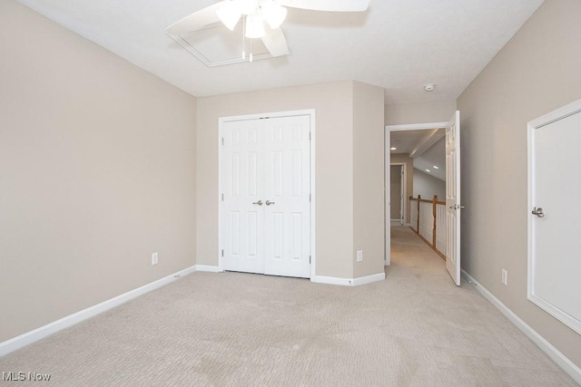 unfurnished bedroom with a closet, light colored carpet, baseboards, and ceiling fan