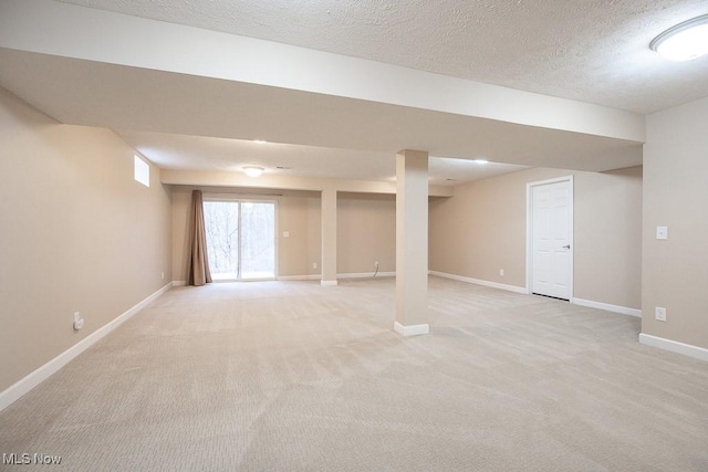 basement featuring light colored carpet, baseboards, and a textured ceiling