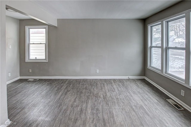 empty room featuring dark wood-type flooring, visible vents, and baseboards