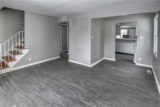 unfurnished living room with dark wood finished floors, visible vents, and baseboards