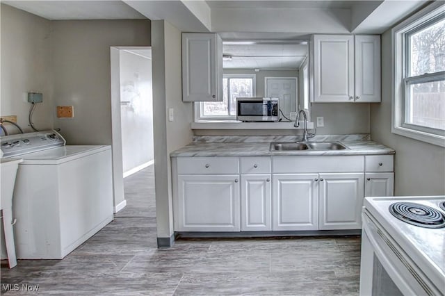 kitchen with light countertops, stainless steel microwave, white cabinets, a sink, and washer / dryer