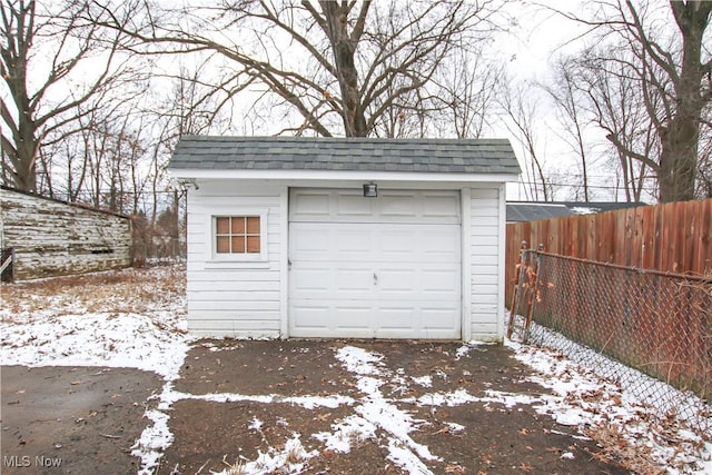 snow covered garage featuring a garage and fence