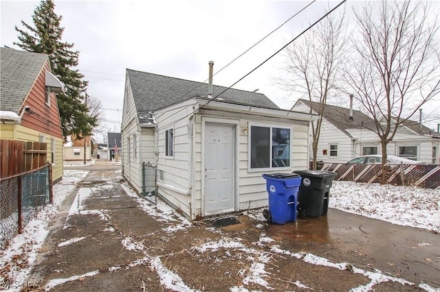 snow covered house featuring fence and roof with shingles