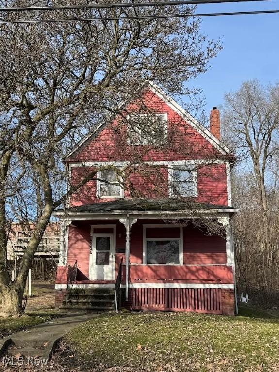 view of front facade featuring covered porch, a front lawn, and a chimney