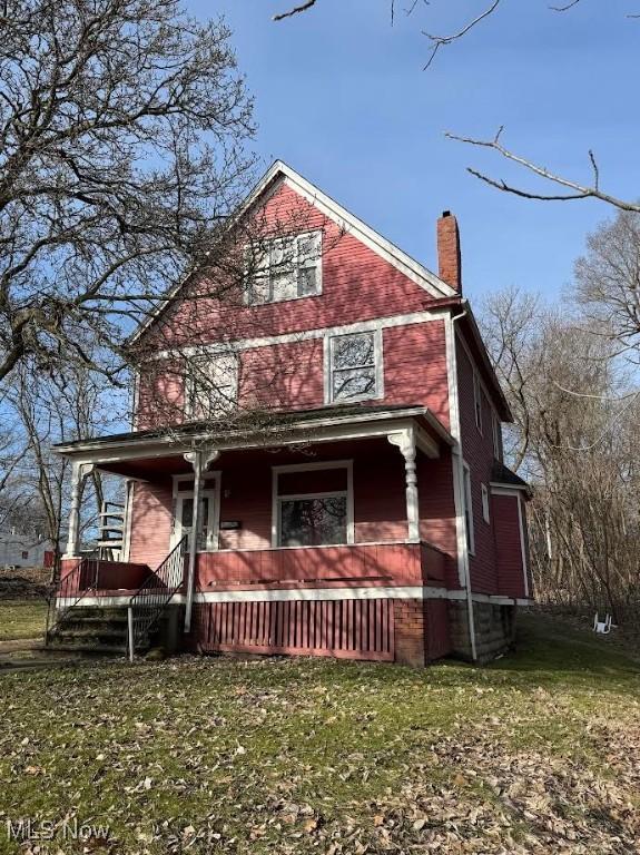 view of front of property with covered porch, a chimney, and a front yard