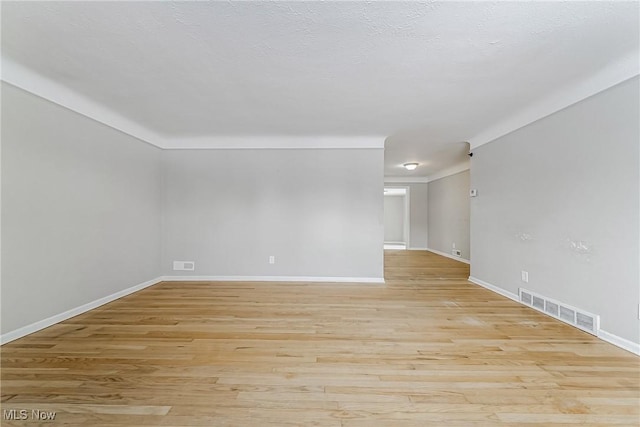 unfurnished room with baseboards, a textured ceiling, visible vents, and light wood-style floors