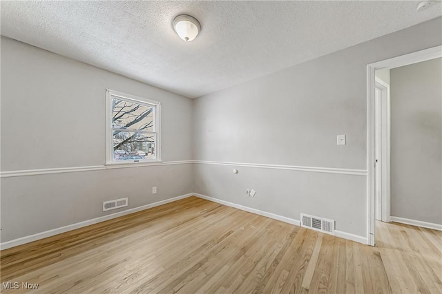 unfurnished room featuring visible vents, a textured ceiling, baseboards, and wood finished floors