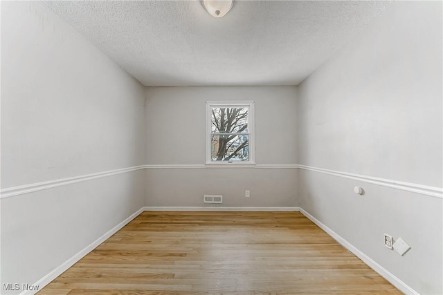 unfurnished room featuring a textured ceiling, wood finished floors, visible vents, and baseboards