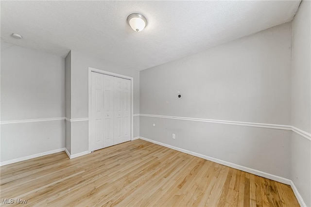 unfurnished bedroom with a textured ceiling, a closet, baseboards, and wood finished floors