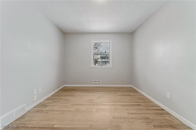 unfurnished room with light wood-type flooring, baseboards, visible vents, and a textured ceiling