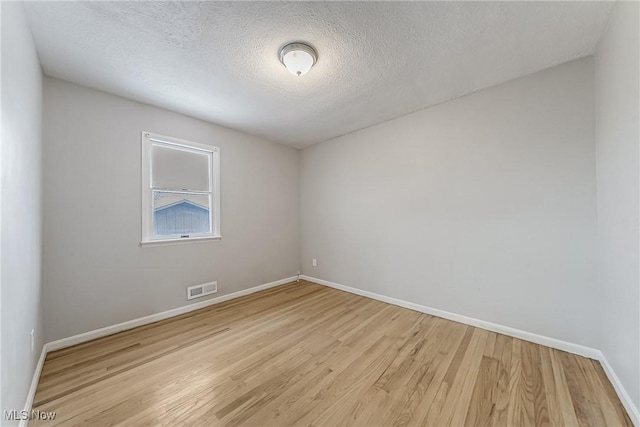 empty room featuring light wood-style floors, baseboards, visible vents, and a textured ceiling