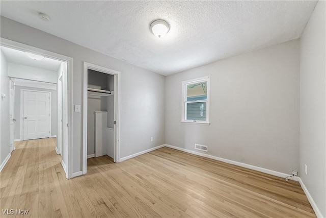 unfurnished bedroom featuring baseboards, visible vents, a textured ceiling, light wood-type flooring, and a closet